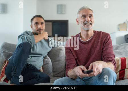 Lächelndes männliches Paar, das zu Hause fernsieht Stockfoto