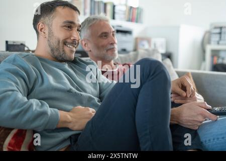 Lächelndes männliches Paar, das zu Hause fernsieht Stockfoto