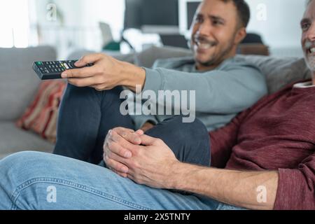 Lächelndes männliches Paar, das zu Hause fernsieht Stockfoto