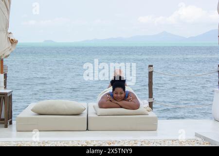 Junge Frau, die sich auf einer Liege in der Nähe der Bucht entspannt Stockfoto