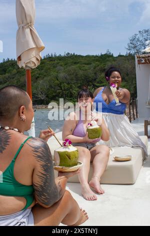 Gruppe fröhlicher Frauen, die Cocktails trinken und sich auf Sonnenliegen entspannen Stockfoto