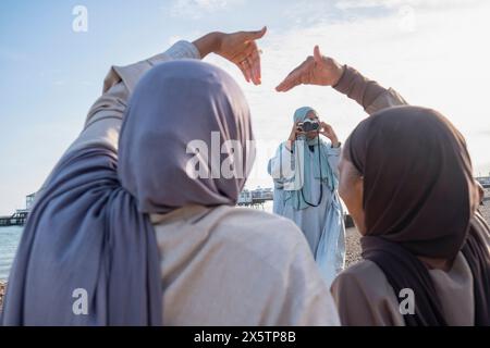 Frau, die muslimische Freunde fotografiert und mit Händen am Strand Herzform macht Stockfoto