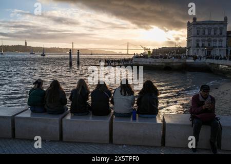 Menschen beobachten in Lissabon, Straßenfotografie - Praca Commercial, Haupthafen am Meer. Sitzen und den Sonnenuntergang über Brücke und Rive am 25. April beobachten Stockfoto