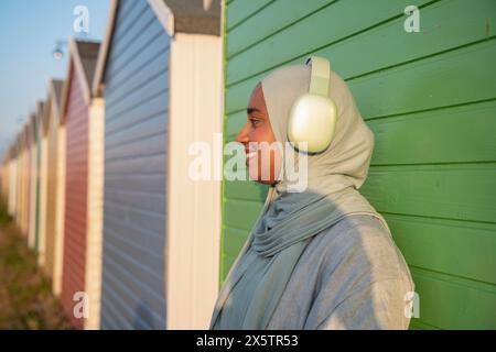 Seitenansicht einer muslimischen Frau, die am sonnigen Tag Musik hört Stockfoto