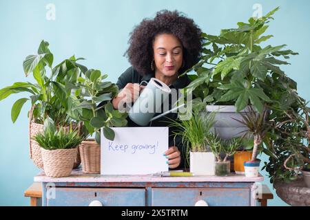 Studio-Porträt einer lächelnden Frau mit Topfpflanzen, Gießkanne und Schild Stockfoto