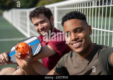 Porträt zweier lächelnder Männer, die auf dem Pickleball-Platz sitzen Stockfoto