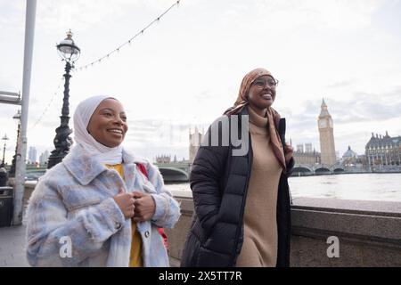 Großbritannien, London, Junge weibliche Touristen in Hijabs, die entlang der Themse spazieren Stockfoto