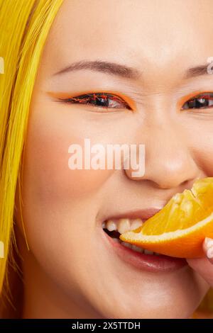 Junge Frau mit Orangenschminke, die Orangenfrüchte isst Stockfoto