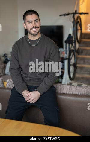 Ein lächelnder junger Mann sitzt zu Hause im Wohnzimmer Stockfoto