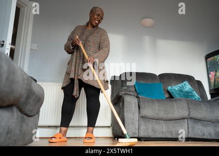 Reife Frau, die im Wohnzimmer den Boden fegt Stockfoto