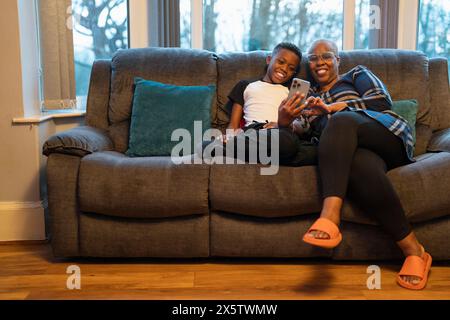 Großmutter und Enkel mit Smartphone sitzen auf Sofa Stockfoto