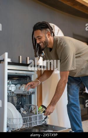 Mann mit Dreads, der Geschirrspüler lädt Stockfoto