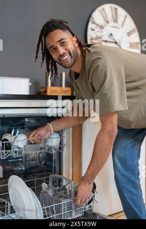 Mann mit Dreads, der Geschirrspüler lädt Stockfoto