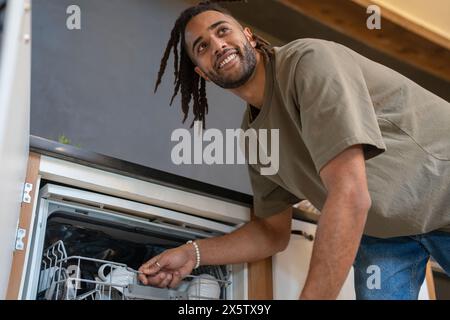 Mann mit Dreads, der Geschirrspüler lädt Stockfoto