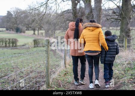 Junge mit Eltern in Winterjacken, die in ländlicher Umgebung spazieren gehen Stockfoto