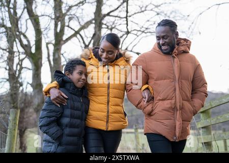 Junge mit Eltern in Winterjacken, die in ländlicher Umgebung spazieren gehen Stockfoto