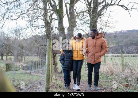 Junge mit Eltern in Winterjacken, die in ländlicher Umgebung spazieren gehen Stockfoto