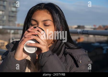 Porträt einer Frau im Jackentrinken aus Einwegbecher im Freien Stockfoto