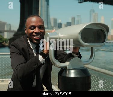 USA, New York City, lächelnder Mann im Anzug an Münzferngläsern Stockfoto