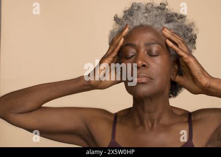 Atelieraufnahme einer Reifen Frau mit geschlossenen Augen und Kopf in den Händen Stockfoto
