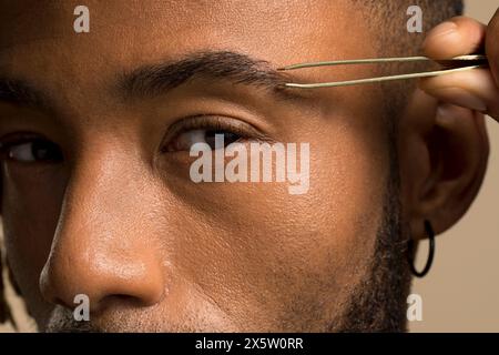 Atelierporträt eines jungen Mannes, der die Augenbraue zupft Stockfoto