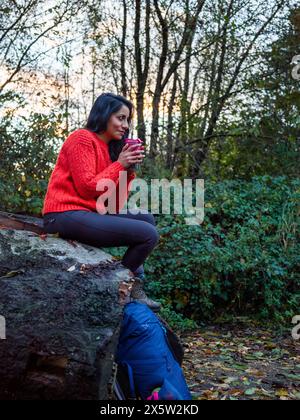 Weibliche Wanderer sitzt auf Felsen und trinkt heißes Getränk Stockfoto