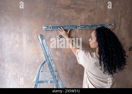 Frau, die eine Wasserwaage an der Wand benutzt Stockfoto