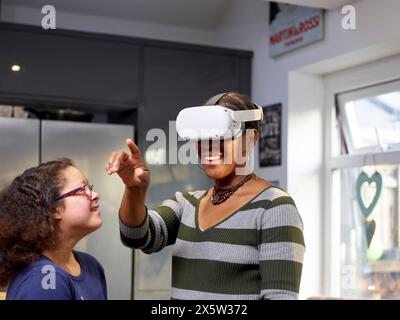 Mädchen mit Down-Syndrom, das Mutter mit VR-Schutzbrille ansieht Stockfoto