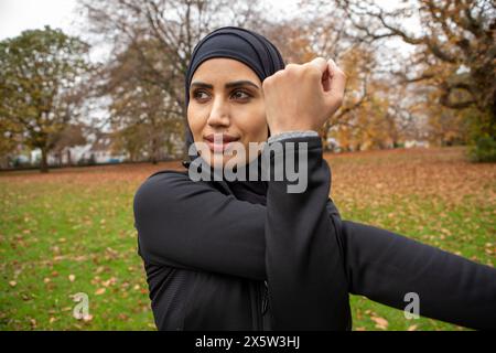 Frau in schwarzer Sportkleidung und Hijab, die sich im Park ausdehnt Stockfoto