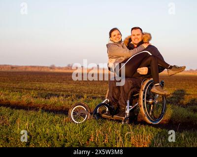 Lächelnder Mann auf Rollstuhl auf dem Feld, der Frau trägt Stockfoto