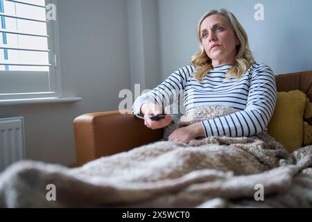 Reife wirtschaftlich inaktive Frau mit Langzeitkrankheiten auf dem Sofa zu Hause und Fernsehen Stockfoto