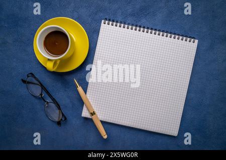 Leeres Spiralnotizbuch mit liniertem Papier, flacher Lay mit Kaffee, Lesebrille und Stift auf blauem, strukturiertem Kunstdruckpapier Stockfoto