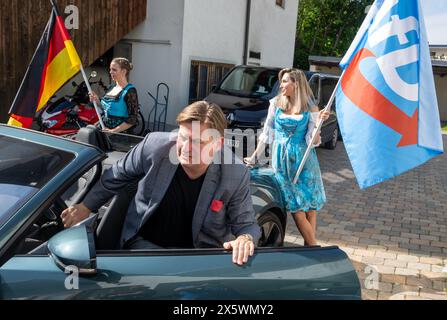 Holzkirchen, Deutschland. Mai 2024. Maximilian Krah, der Spitzenkandidat der AfD für die Europawahlen, steigt bei einer Wahl aus einem Sportwagen aus und wird von zwei Frauen flankiert, die Fahnen schwenken. Die Veranstaltung wurde aufgrund von Protesten nach Holzkirchen verlegt. Quelle: Stefan Puchner/dpa/Alamy Live News Stockfoto