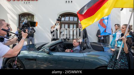 Holzkirchen, Deutschland. Mai 2024. Maximilian Krah, der Spitzenkandidat der AfD für die Europawahlen, sitzt bei einer Wahlveranstaltung in einem Sportwagen und wird von zwei Frauen flankiert, die Fahnen schwenken. Die Veranstaltung wurde aufgrund von Protesten nach Holzkirchen verlegt. Quelle: Stefan Puchner/dpa/Alamy Live News Stockfoto