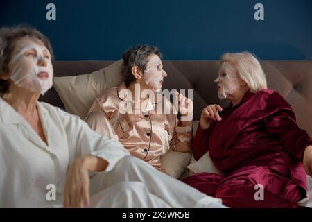 Glückliche ältere Freundinnen mit Baumwollmaske im Gesicht, die sich nett unterhalten Stockfoto