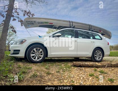 Rosebud, MO, USA - 20. April 2024: Tandemkanu aus Aluminium mit Rennnummern und Aufklebern auf Dachgepäckträgern von Volkswagen SUV auf einem Waldparkplatz. Stockfoto