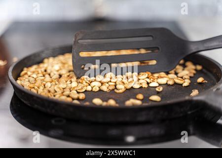 Kaffeebohnen werden in einer gusseisernen Pfanne geröstet. Grüne Körner werden mit einem Teigschaber vermischt. Ausgewählter Fokus. Hochwertige Fotos Stockfoto