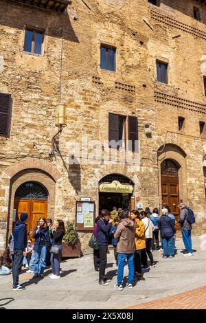 Touristen stehen vor der berühmten Gelateria Dondoli Gelato Shop und essen Eis in der historischen Stadt San Gimignano in der Toskana, Italien. Stockfoto