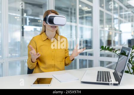 Engagierte junge weibliche Profi, die VR-Headset verwenden, um von einer hellen Büroumgebung aus an einem virtuellen Meeting teilzunehmen. Stockfoto
