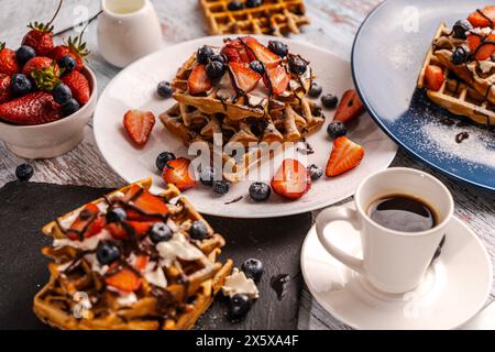 Köstliche belgische Waffeln mit Puderzucker und Beeren auf Tellern und eine Tasse Kaffee. Süßes Essen. Nachtisch. Essen servieren. Hochwertige Fotos Stockfoto