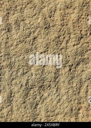 Braune unebene Wand, Textur, Hintergrund. Relief felsige und schattige Oberfläche aus Granitstein. Vulkanisches Gestein von hellbrauner Farbe in der Stadtentwicklung Stockfoto