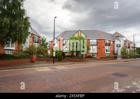 Apartmentkomplex entlang einer Backsteinstraße an einem bewölkten Tag. Vor den Gebäuden befindet sich eine Bushaltestelle. Stockfoto