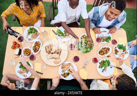 Blick von oben auf glückliche Menschen am Esstisch mit Weingläsern und Essen im Freien. Stockfoto