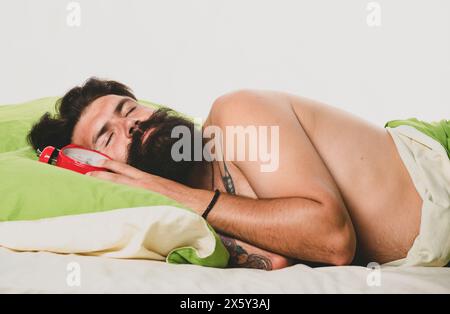 Alarmkonzept. Schöner Mann, der im Bett schläft. Müde und faul Person langsam posiert allein. Braucht etwas Ruhe. Junger Mann schläft auf weichen Kissen im Bett Stockfoto