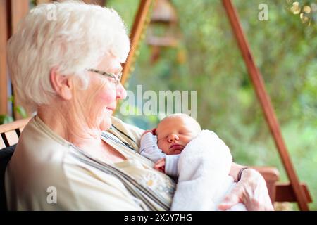 Großmutter trifft neugeborenes Enkelkind. Ältere Frau, die ein kleines Baby hält. Oma mit Kleinkind-Enkel im sonnigen Sommergarten. Generationen lieben es. Stockfoto