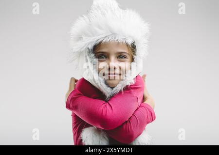 Ein junges Mädchen in einem wunderbaren weißen Winterhut umarmt sich warm, ihre fröhlichen Augen und ihr sanftes Lächeln vermitteln Trost und Glück Stockfoto