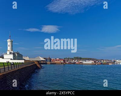 Arbroath Signal Tower mit seinen weiß getünchten Wänden mit Blick auf den Tidal Harbour, mit Menschen auf Bänken entlang des Coastal Path. Stockfoto