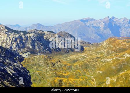 Farbenfrohe Herbstlandschaft vom Durmitor Nationalpark, Montenegro: Aus der Vogelperspektive auf ein grasbewachsenes Tal, die Durmitor Ringstraße und die hohen Berge dahinter Stockfoto