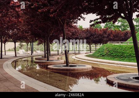 Stadtpark mit modernem Design und Bäumen mit rotem Laub und künstlichem Teich Stockfoto