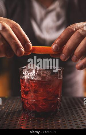 Nahaufnahme der Hände eines Barkepers, die einen lebhaften Cocktail mit Orangenschalen garnieren Stockfoto
